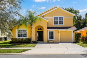 A two-story yellow house with a black front door, a garage, and a well-maintained lawn. - Our Happy Place! FREE Pool Heat (Davenport)