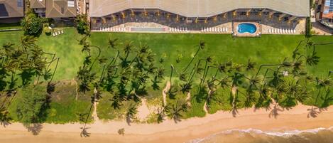 An aerial view of a hotel with a pool, beach, and parking lot.