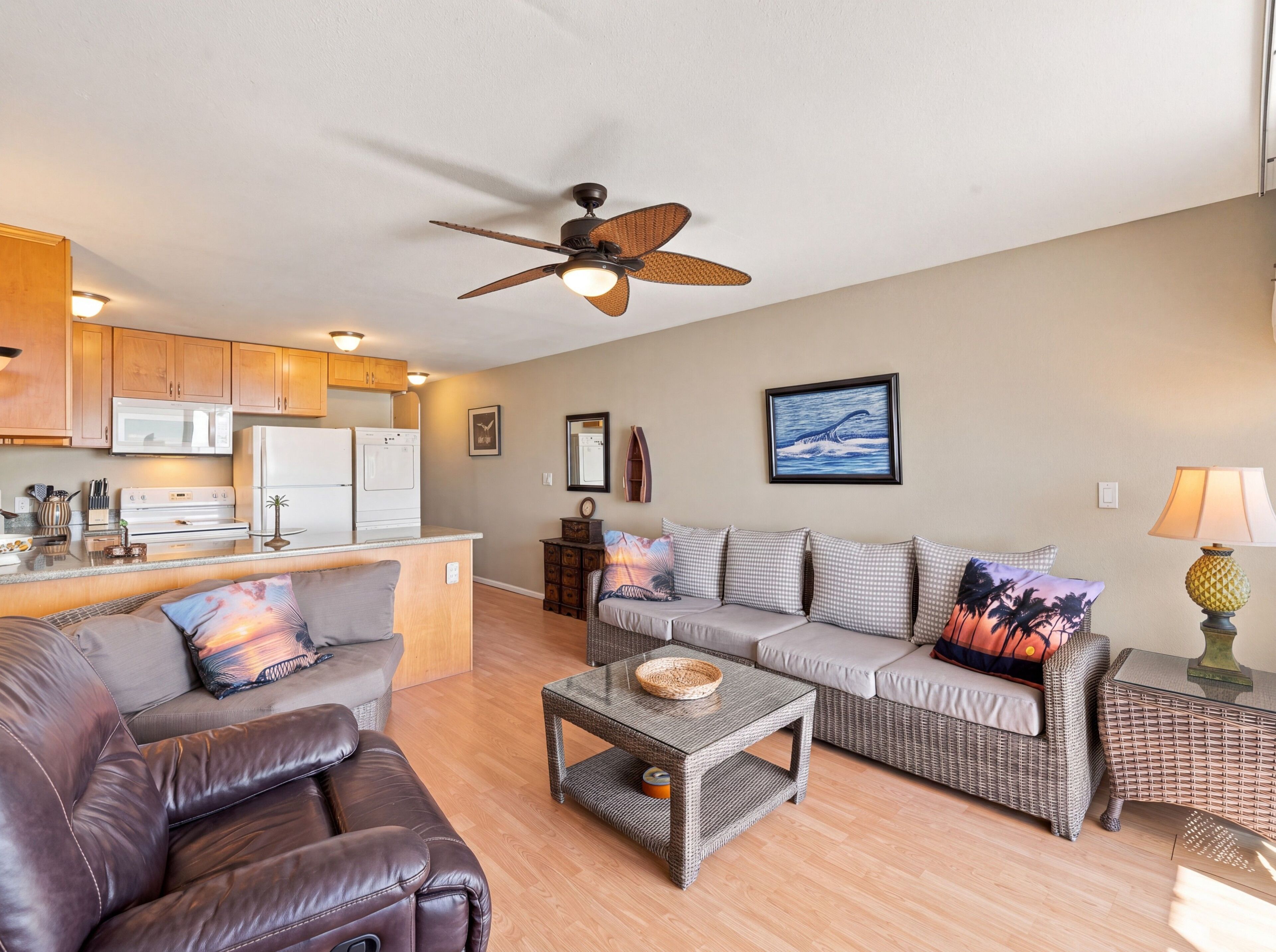 A modern living room with a sofa, a leather couch, a dining area with a kitchen in the background, and a ceiling fan.