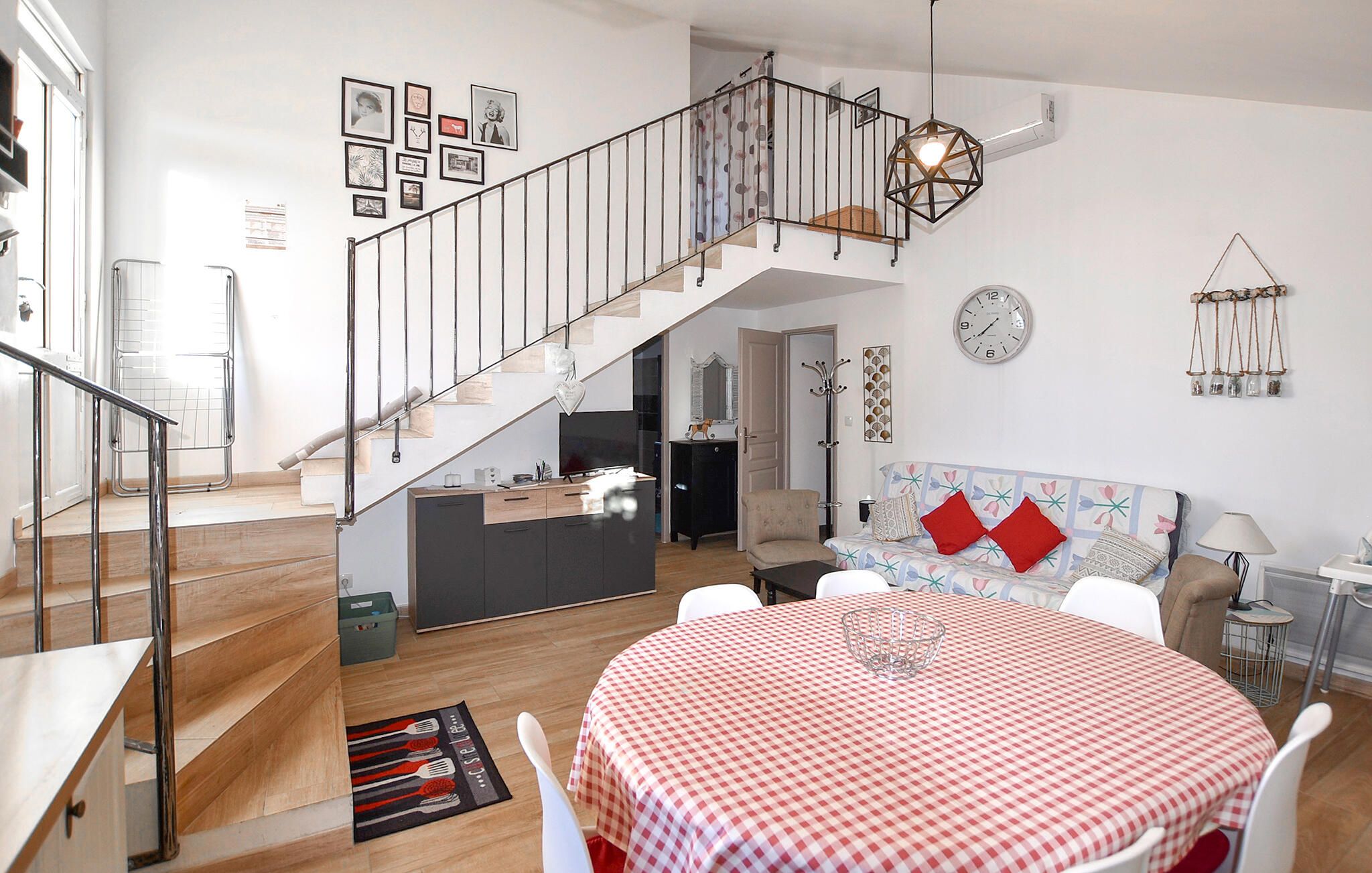 A modern living room with a staircase, a dining area with a checkered tablecloth, and a kitchen area.