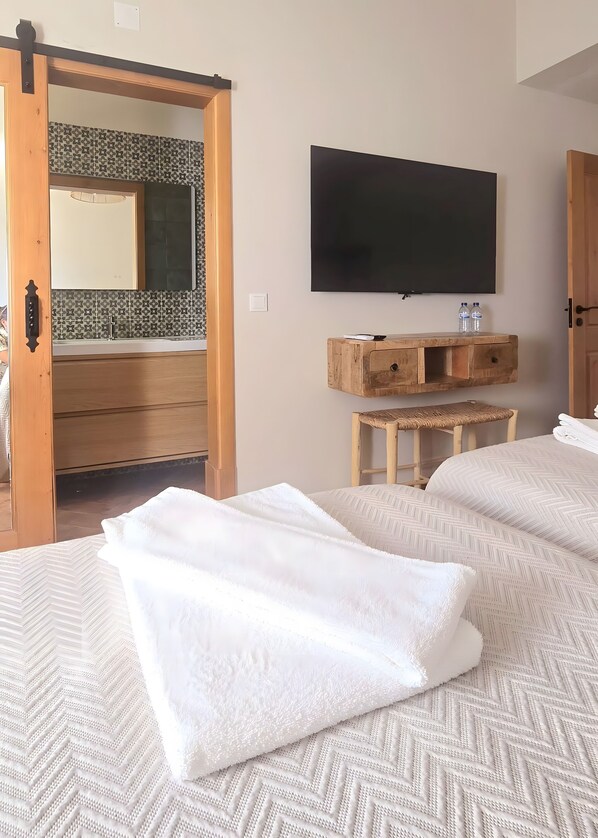 A hotel room with a bed, a TV, a wooden dresser, and a bathroom with a patterned tile backsplash.