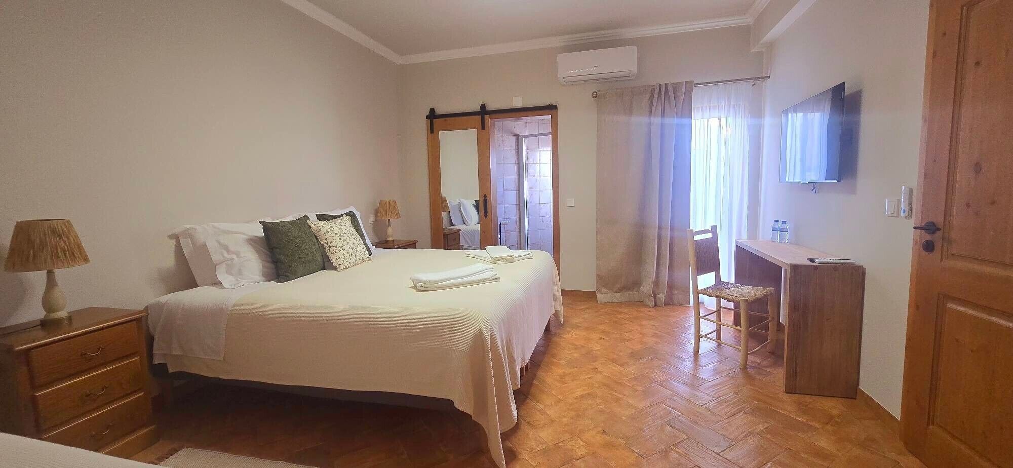 A bedroom with a bed, bedside table, lamp, and a desk with a chair.