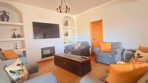 A living room with a fireplace, sofas, a coffee table, and a TV mounted on the wall. - Villa 'Casas Do Monte I - T3' with Shared Pool, Private Terrace and Wi-Fi (Moinhos de vento)