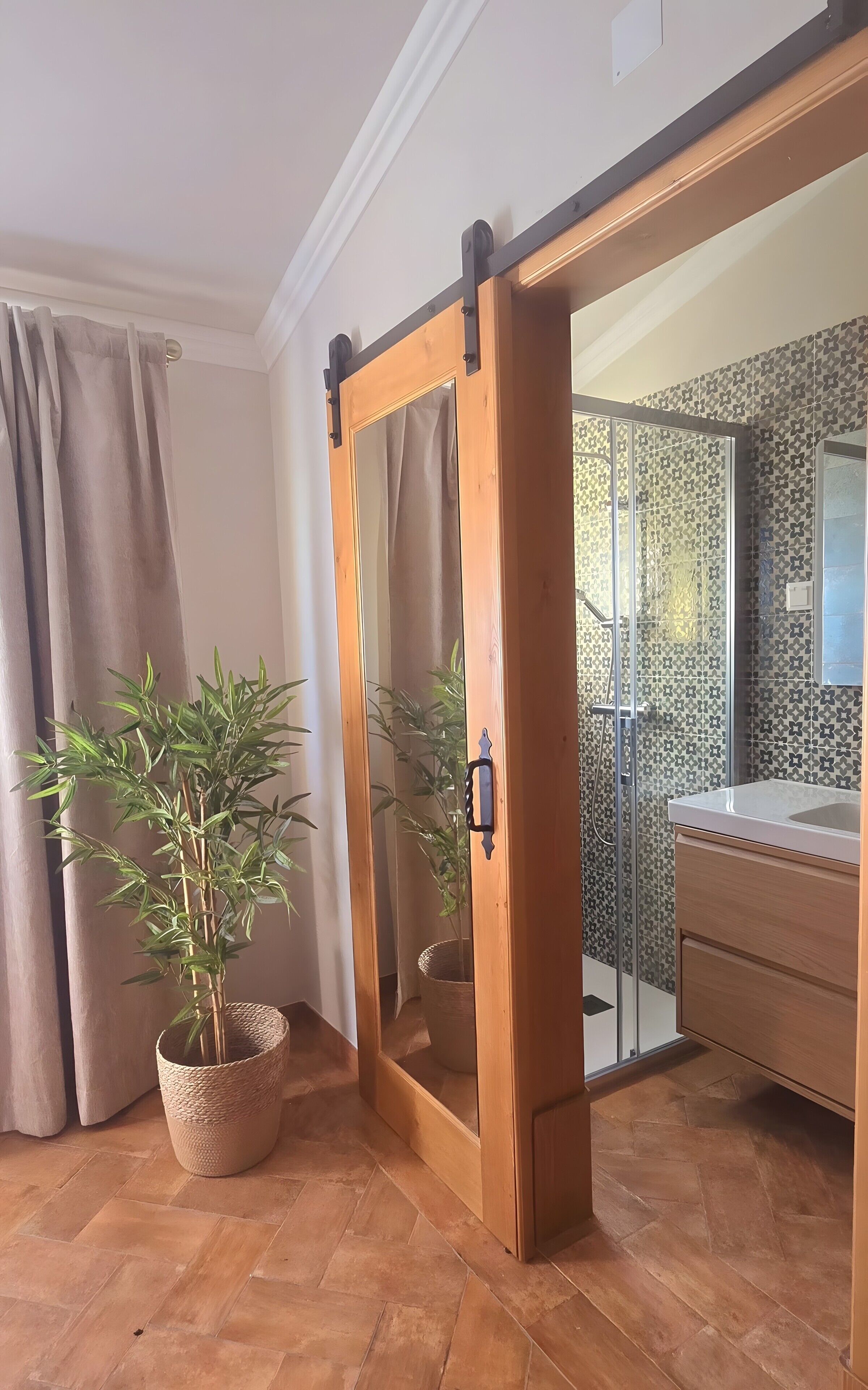 Une pièce dotée d’une porte coulissante donnant sur une salle de bain, d’une plante en pot et d’un sol carrelé.