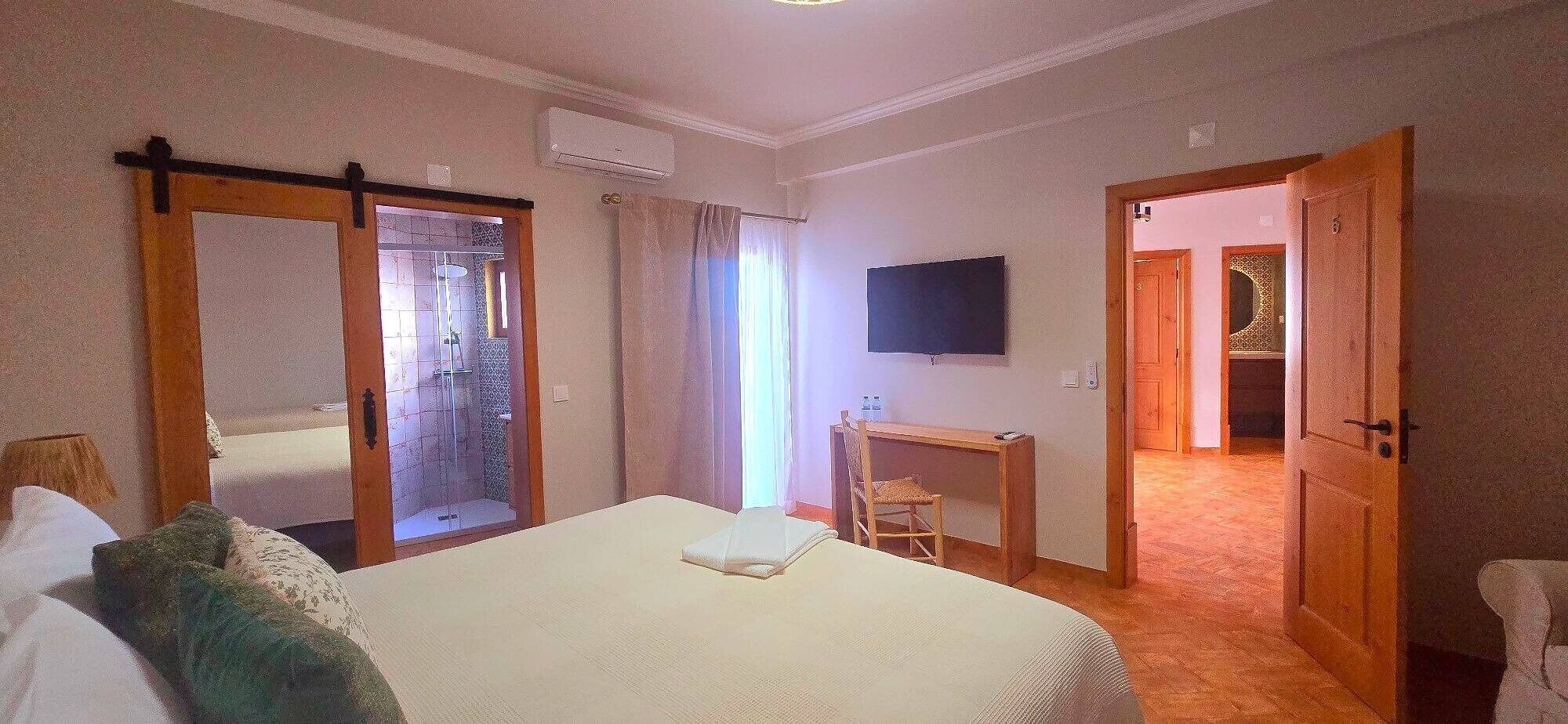 A hotel room with a bed, a desk, a TV, and a shower area.