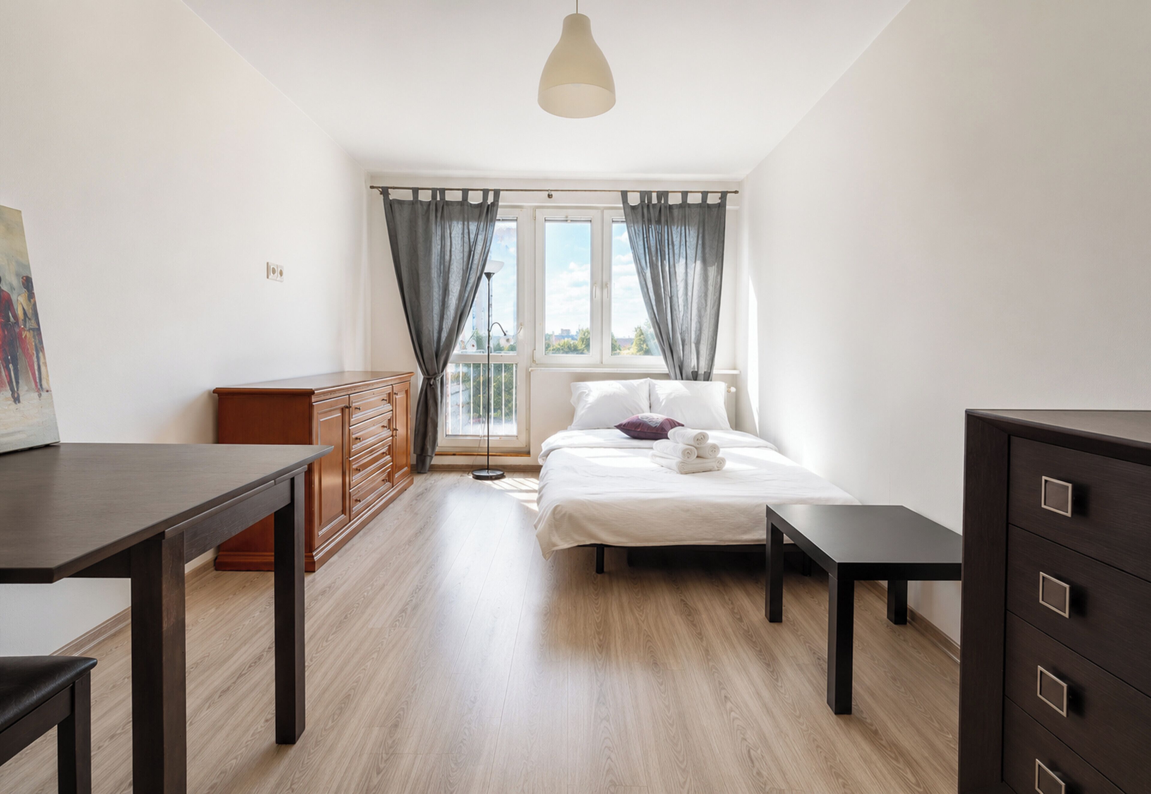 Ein Schlafzimmer mit einem Bett, Nachttischen, einer Kommode, einem Schreibtisch und einem Fenster mit Vorhängen.