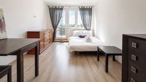 Un dormitorio con cama, mesitas de noche, cómoda, escritorio y ventana con cortinas.
