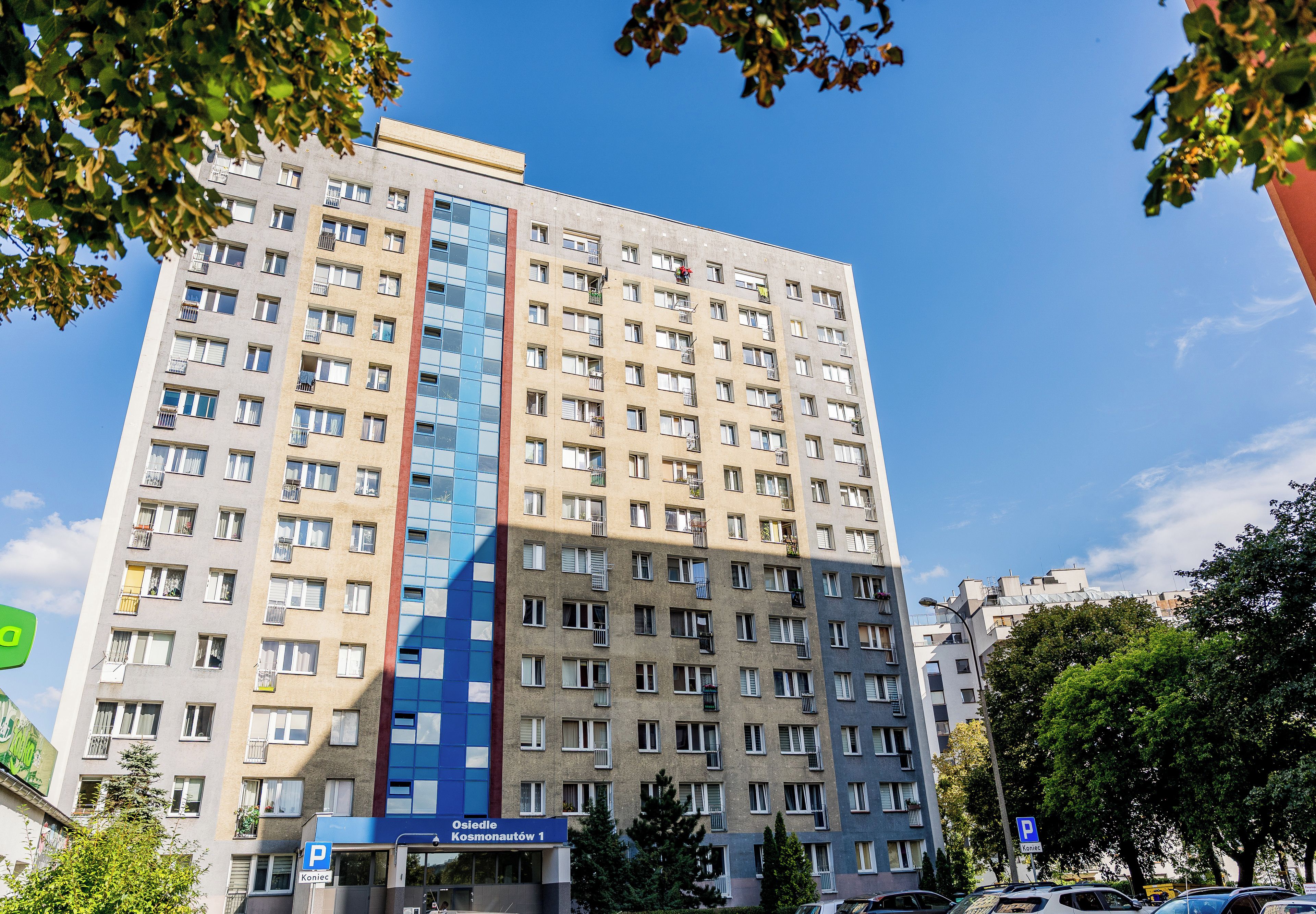 Ein mehrstöckiges Hotel mit einer zentralen, blauen Glasfassade, mehreren Balkonen und einem Schild, das freie Parkplätze anzeigt.