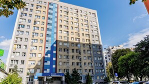 Un hotel de varios pisos con fachada central de vidrio azul, varios balcones y un letrero de estacionamiento que indica disponibilidad.