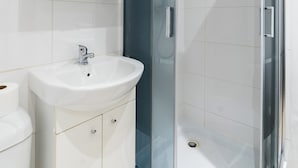 Un baño moderno con lavamanos blanco, espejo y cabina de ducha de vidrio.