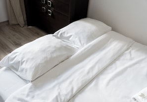 Ein Bett mit weißer Bettwäsche in einem Zimmer mit Holzboden und einem dunklen Kommodenstück.