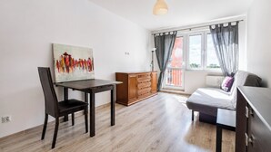 Una habitación con una mesa de comedor, sillas, un cuadro, un sofá, una ventana con cortinas y una lámpara colgante.