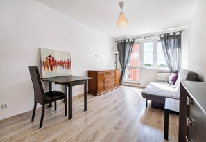 Ein Zimmer mit Esstisch, Stühlen, einem Gemälde, einer Couch, einem Fenster mit Vorhängen und einer Pendelleuchte.