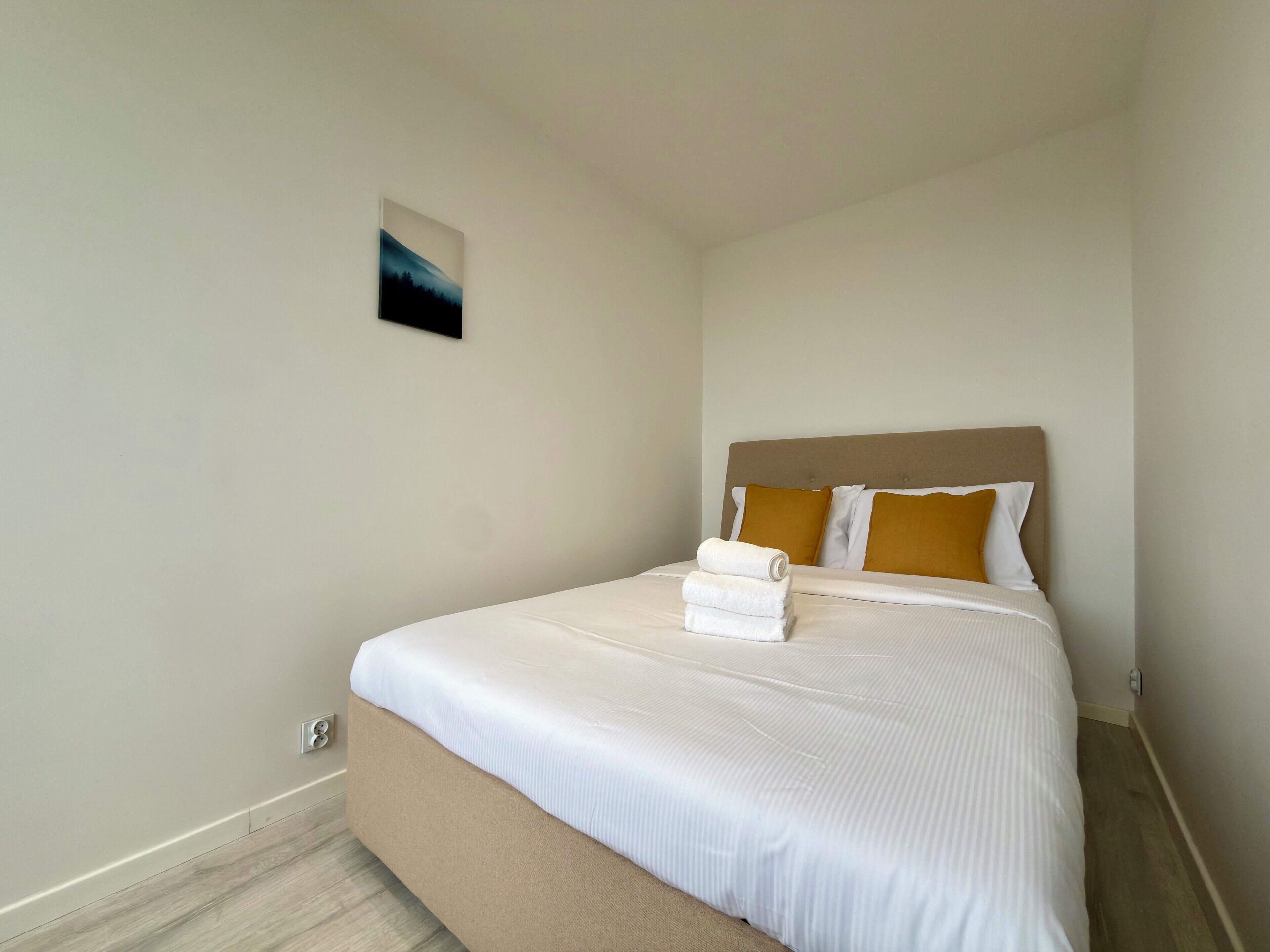 Une chambre d’hôtel avec un lit, une tête de lit et un petit tableau accroché au mur.