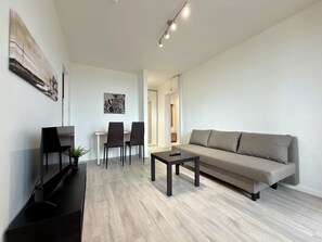 Ein modernes Wohnzimmer mit einer Couch, zwei Sesseln, einem Couchtisch und einem Flachbildfernseher.