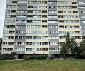 Ein mehrstöckiges Wohngebäude mit Balkonen, nummerierten Wohnungen und einer Rasenfläche mit Fahrrädern.