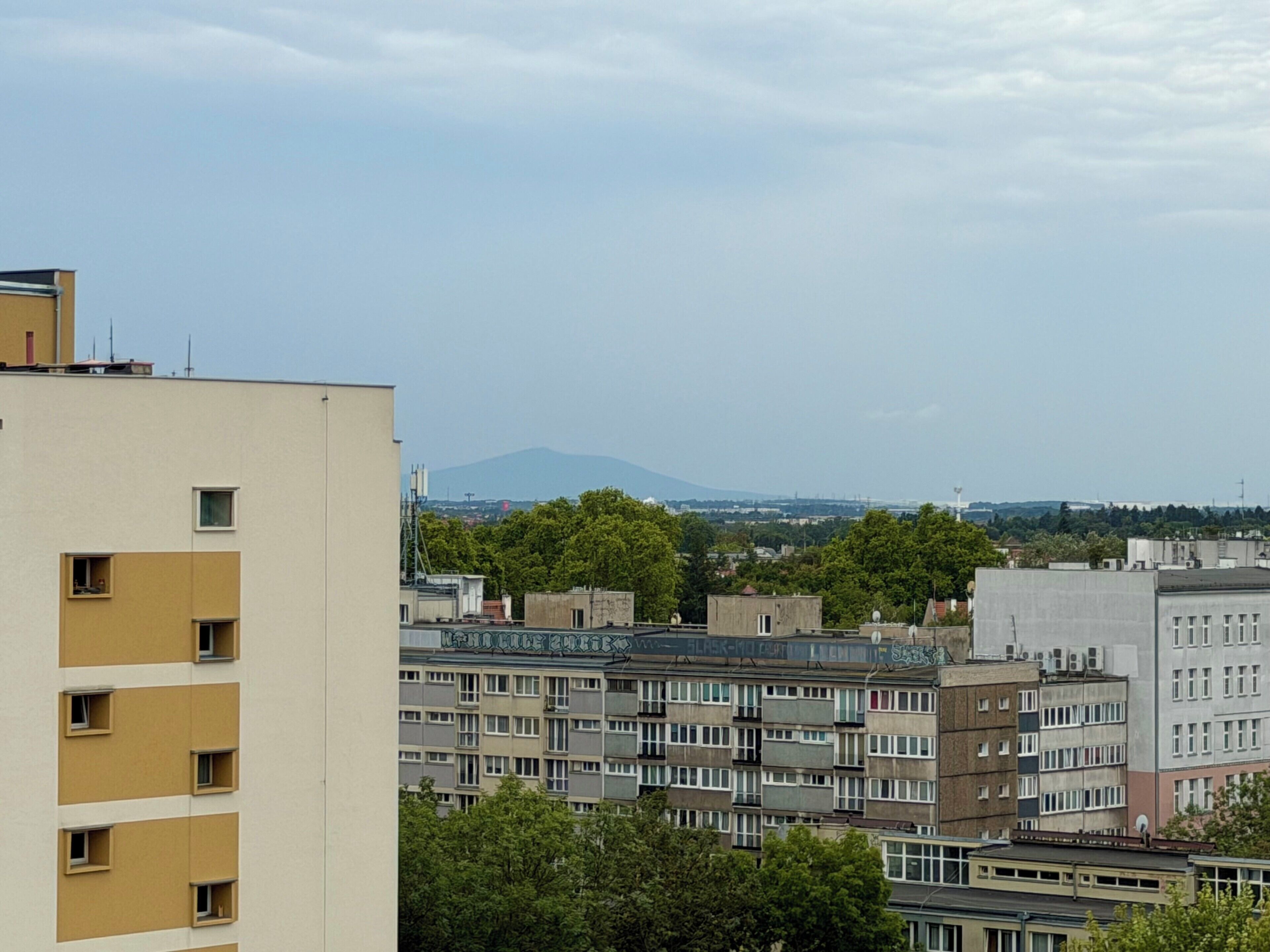 Un edificio residenziale a più piani con balconi, tetto piatto e vista su una montagna in lontananza.