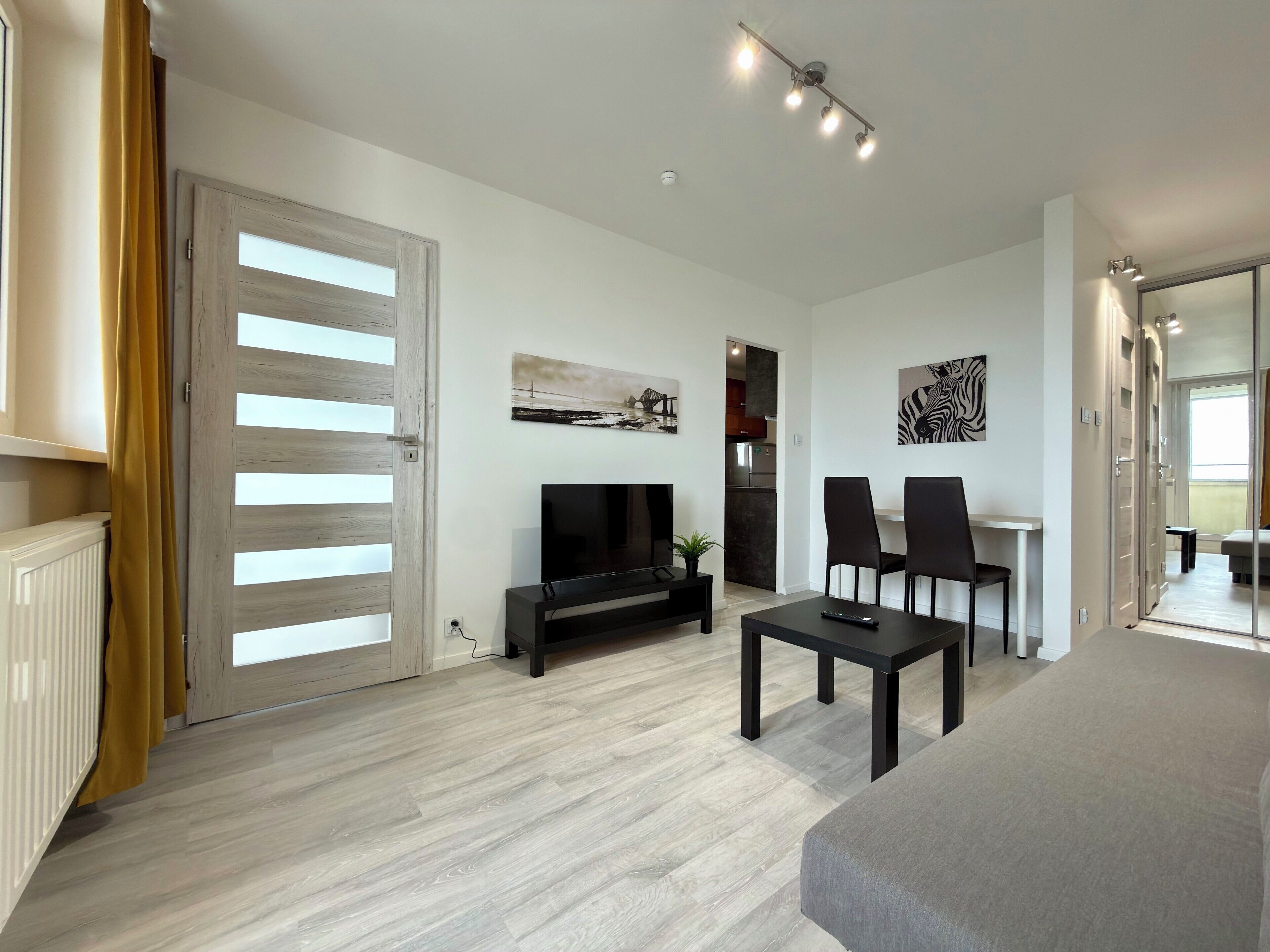 A modern living room with a fireplace, a flat-screen TV, a dining area with chairs, and a kitchen in the background.