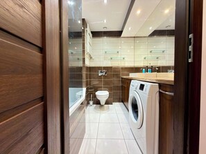 Een moderne badkamer met een wasmachine, toilet en douchecabine met glazen wanden.