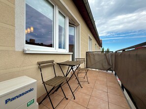 Een balkon met een tafel en stoelen, een Panasonic koelkast, en uitzicht op de lucht.