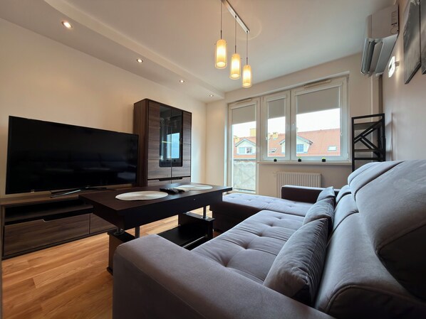 Een moderne woonkamer met een flatscreen televisie, een bank, een eettafel met placematen en hanglampen.