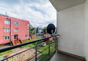 Un balcón con vista a un edificio rojo, una antena parabólica y un área cercada con objetos dispersos.
