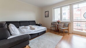 Ein modernes Wohnzimmer mit einem grauen Sofa, einem kleinen runden Tisch mit einem Stuhl und einem großen Fenster mit Blick auf Gebäude.