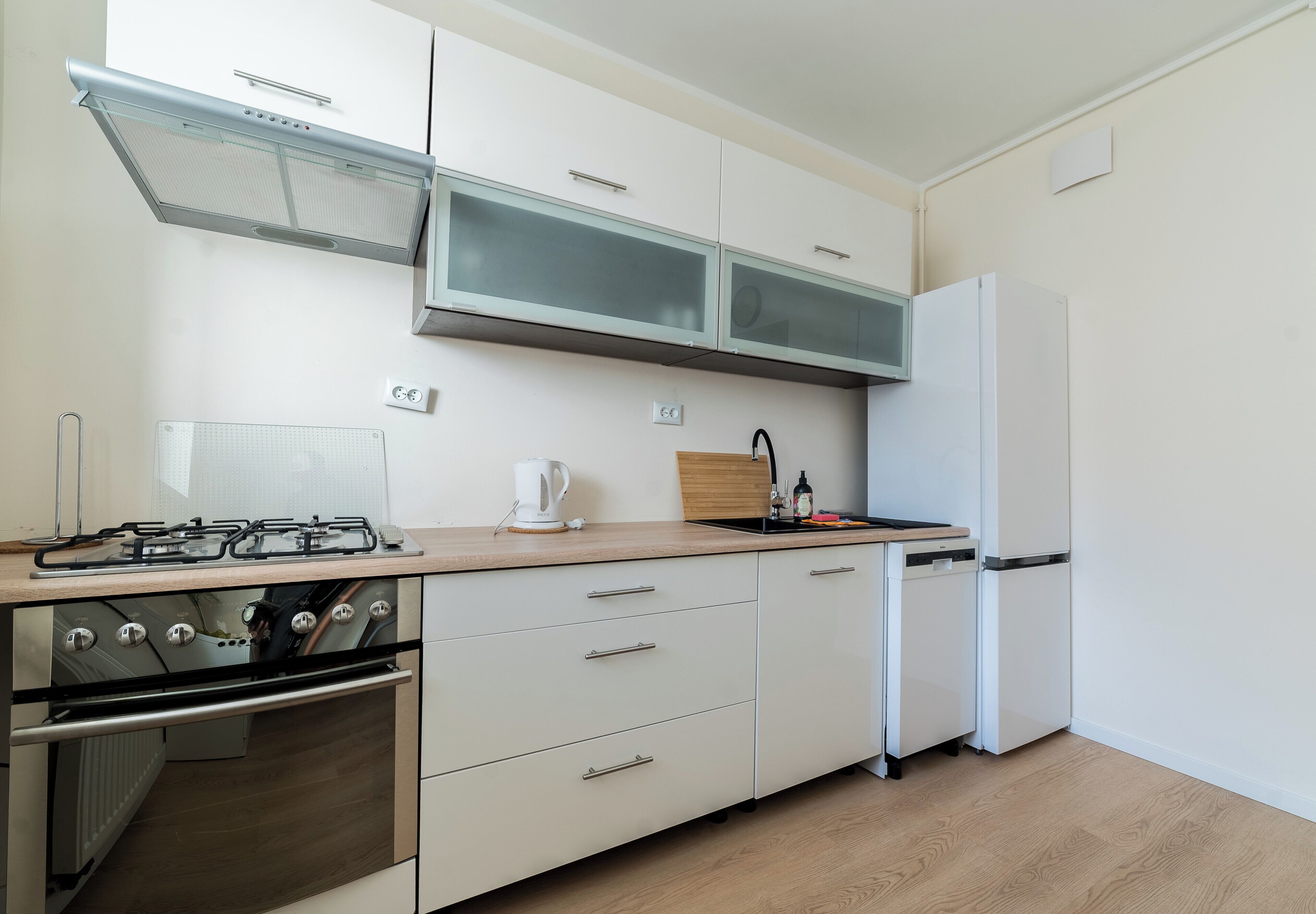 Une cuisine moderne équipée d’une cuisinière à gaz, d’un four, de meubles blancs, d’un micro-ondes encastré et d’un réfrigérateur.