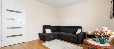 Una sala moderna con un sofá modular, una mesa redonda de madera y una puerta blanca.