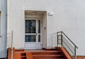 Una puerta blanca con un panel de vidrio, una barandilla metálica y una escalera de ladrillo que sube hacia una entrada numerada.