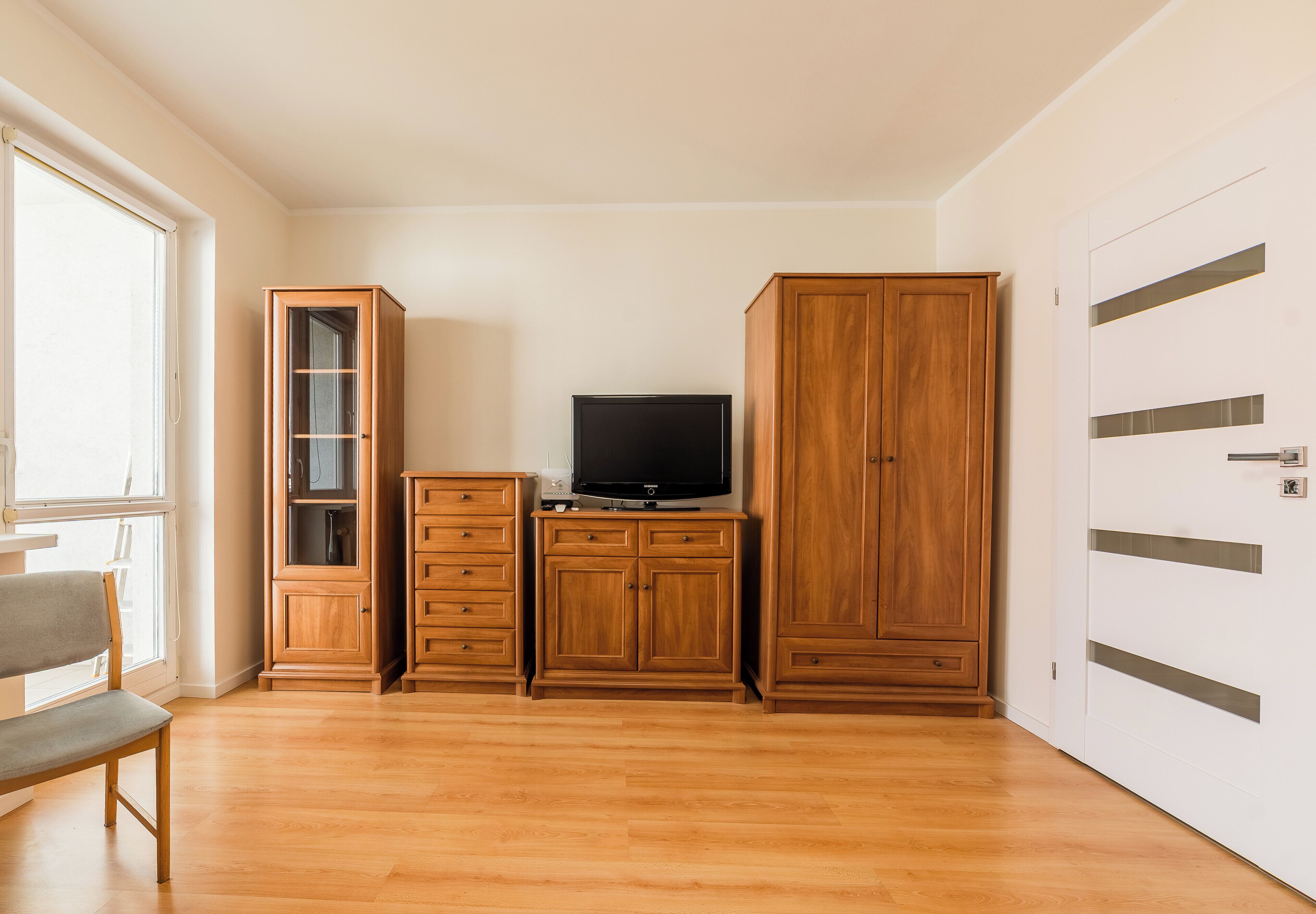 A room with a wooden cabinet, a television on top, a bench, and a door with a handle.