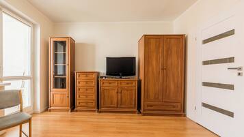 A room with a wooden cabinet, a television on top, a bench, and a door with a handle.