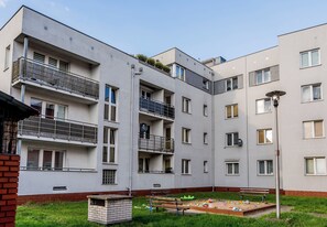 Ein mehrstöckiges Wohngebäude mit Balkonen, einer kleinen Gartenanlage mit einer Bank und einer Straßenlaterne.