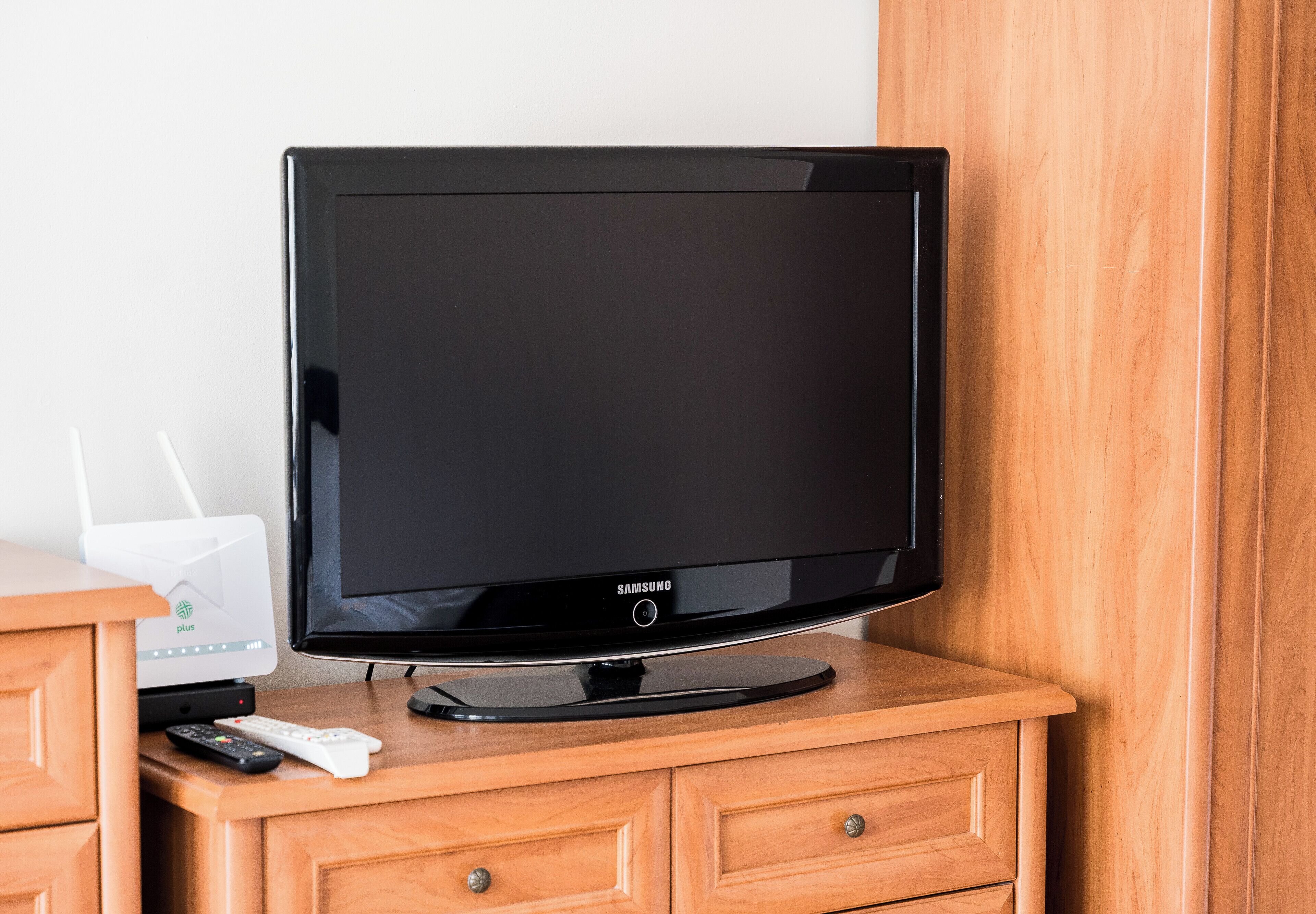 Un televisor de pantalla plana sobre un mueble de madera, con un control remoto y una regleta.