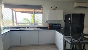 Cozinha com armários brancos, bancada preta, pia, micro-ondas e geladeira.