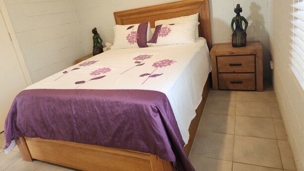 Quarto com cama de madeira, mesa de cabeceira, cômoda e prateleira na parede.