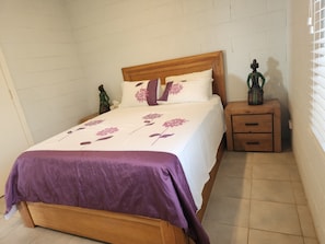 A bedroom with a wooden bed, a nightstand, a dresser, and a wall-mounted shelf.