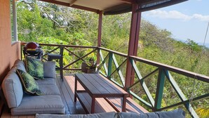 Uma área de estar coberta ao ar livre, com um deck de madeira, um banco acolchoado e uma mesa.