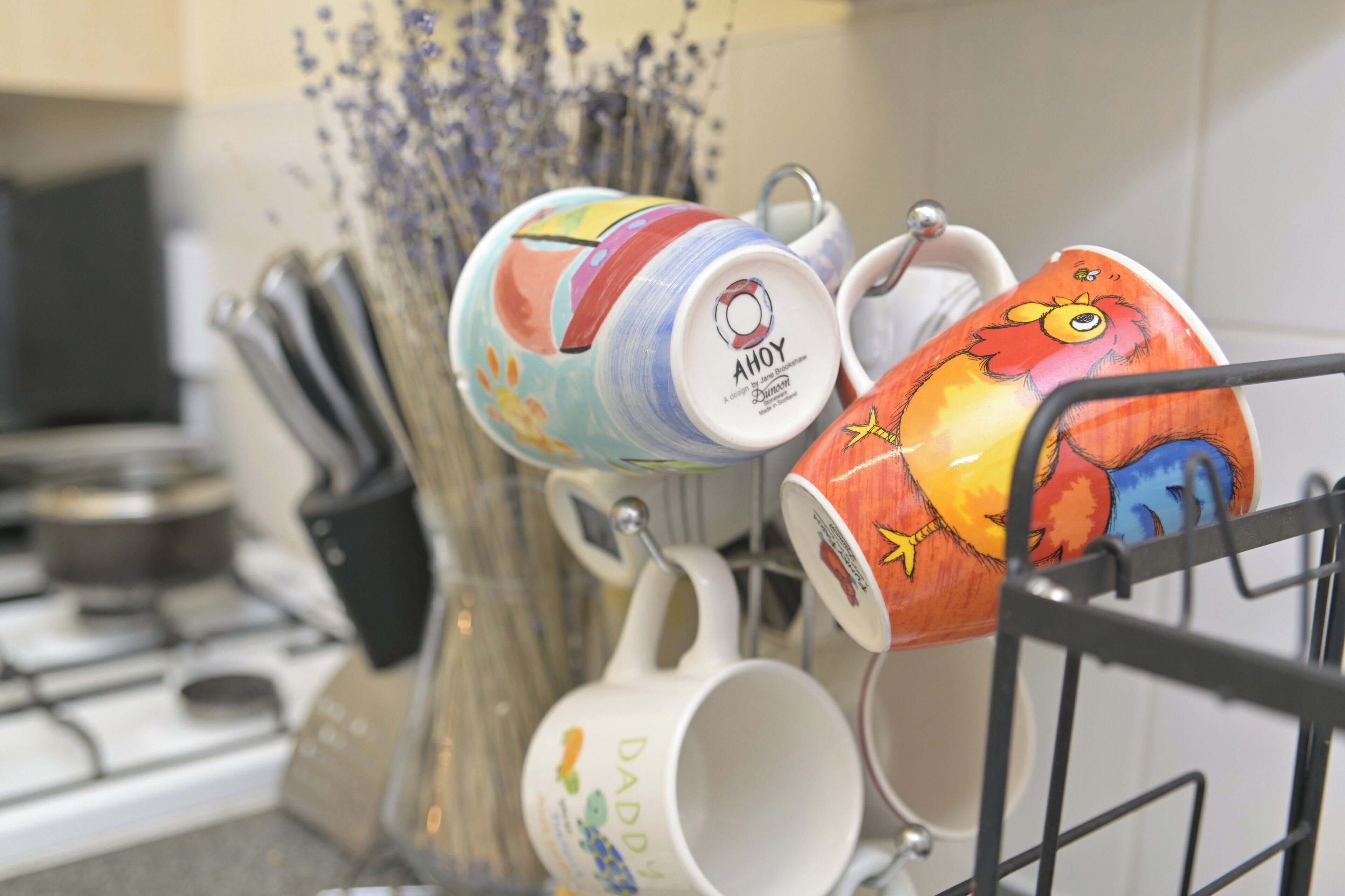 Une cuisine équipée d’une cuisinière, d’un porte-ustensiles et d’une étagère où sont rangées des tasses en céramique aux couleurs vives.