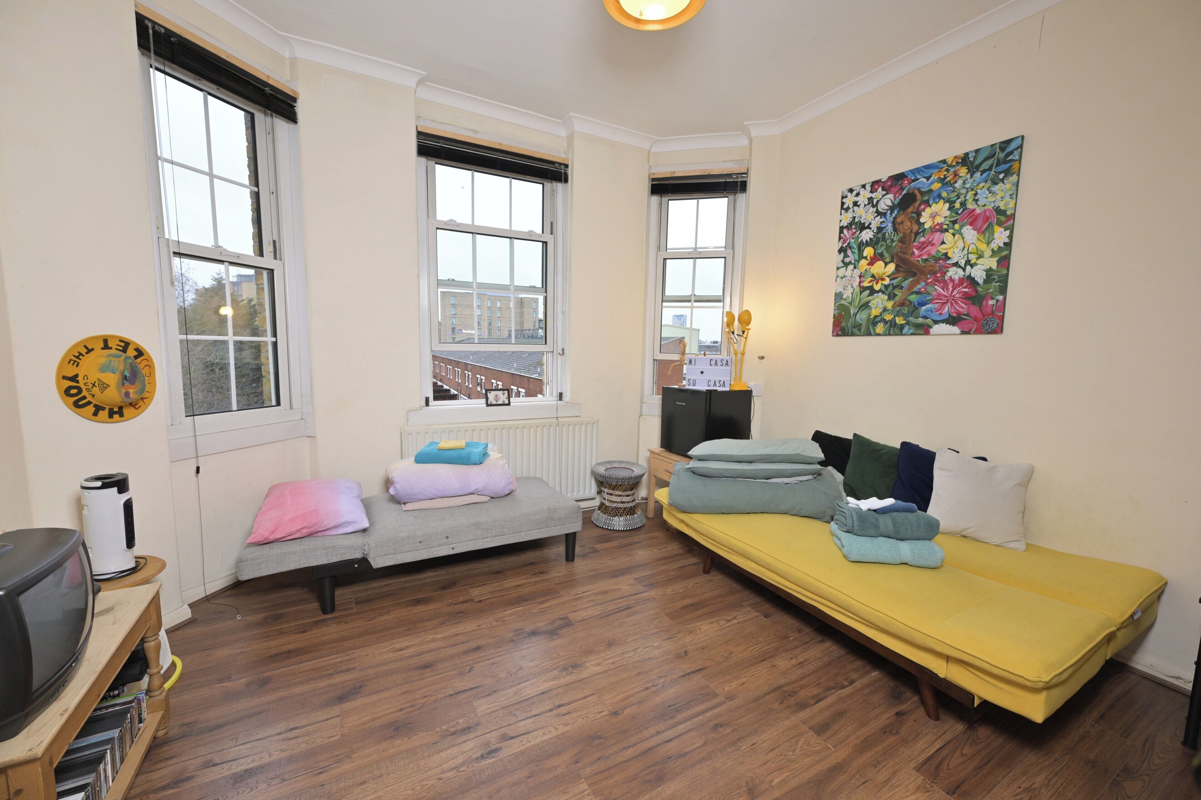 A compact living space with a sofa, a small bed, a television, and a painting on the wall.