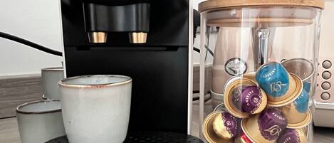 A coffee maker with a cup and a container of coffee capsules.