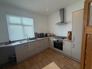 A modern kitchen with a built-in oven, a stainless steel range hood, and a window with blinds. - 3 bedroom Apartment 2 up to 5 people Free parking (Blackpool)