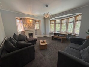 Ein Wohnzimmer mit Kamin, zwei Sofas, einem Couchtisch und großen Fenstern mit Jalousien.