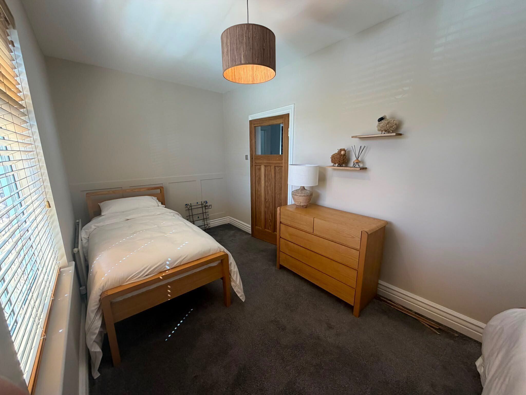A bedroom with a bed, a dresser, a hanging light fixture, and a door.