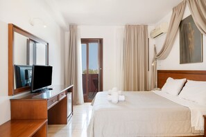 Habitación de hotel con cama, escritorio con televisor, espejo, ventana con cortinas y unidad de aire acondicionado.