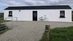 A white building with a black door and windows, a bicycle parked in front, and a gravel driveway. - Seaside Retreat Cottage in Carrowmenagh (Carrowmenagh)