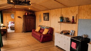 A cozy cabin interior with a wooden floor, a red leather sofa, a kitchen area with a stove, and a dining table with a vase of flowers. - Seaside Retreat Cottage in Carrowmenagh (Carrowmenagh)