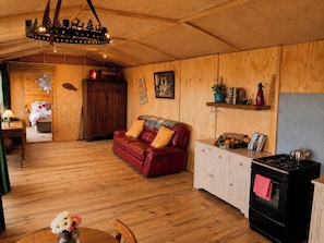 L’intérieur d’un chalet accueillant, avec un plancher en bois, un canapé en cuir rouge, un coin cuisine équipé d’une cuisinière et une table à manger agrémentée d’un vase de fleurs.