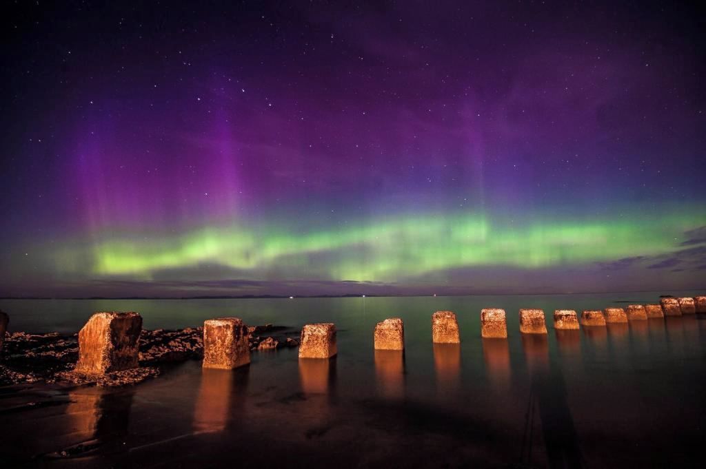 A night scene with the Northern Lights over a calm body of water, reflecting the lights.