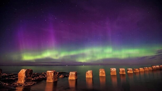 A night scene with the Northern Lights over a calm body of water, reflecting the lights. - Seaside Retreat Cottage in Carrowmenagh (Carrowmenagh)
